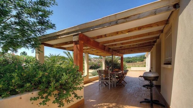Une terrasse extérieure dotée d’une pergola en bois, d’une table avec des chaises et d’un barbecue.