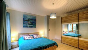 Ein Schlafzimmer mit einem Bett, Nachttischlampen, einem Gemälde, einem Spiegel und Holzböden.
