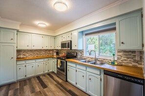 A kitchen with light blue cabinets, a stainless steel dishwasher, a microwave, and a window with a view of greenery. - Charming Escape  and cozy  place near everything (Surrey)