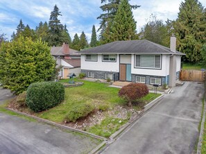A two-story house with a front yard, driveway, and surrounding trees. - Charming Escape  and cozy  place near everything (Surrey)
