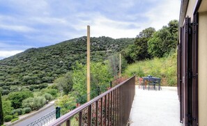 Ein Balkon mit Blick auf eine Hügelkuppe, ein Tisch mit Stühlen und ein Gebäude mit einer Tür.