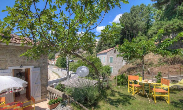 Ein Steinhaus mit einer Tür, einem kleinen Tisch mit Stühlen und einem kugelförmigen Objekt im Garten.
