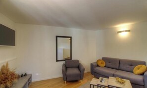Ein modernes Wohnzimmer mit einem grauen Sessel, einer grauen Couch mit zwei Kissen, einem kleinen Tisch mit einer Vase und einem Spiegel an der Wand.