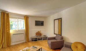 Ein Wohnzimmer mit einer Couch, einem an der Wand montierten Fernseher, einer Heizung und einem Fenster mit Vorhängen.