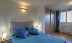 Ein Schlafzimmer mit Bett, Nachttischlampen, einem Fenster mit Vorhängen und einer Heizung.