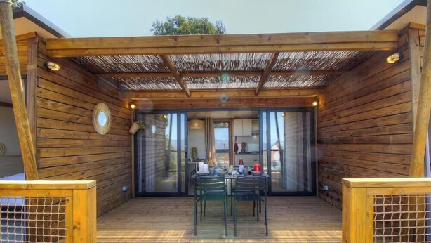 Une terrasse en bois avec une table et des chaises, une pergola et une vue sur l’intérieur.