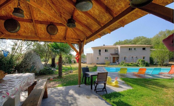 Un espace extérieur abrité avec une piscine, une table, des chaises et un bâtiment en arrière-plan.