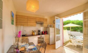 Eine kompakte Küche mit Holzausstattung, einer Mikrowelle und einem Kühlschrank. Es gibt einen Essbereich mit Tisch und Stühlen, und eine Terrasse mit Sonnenschirm.