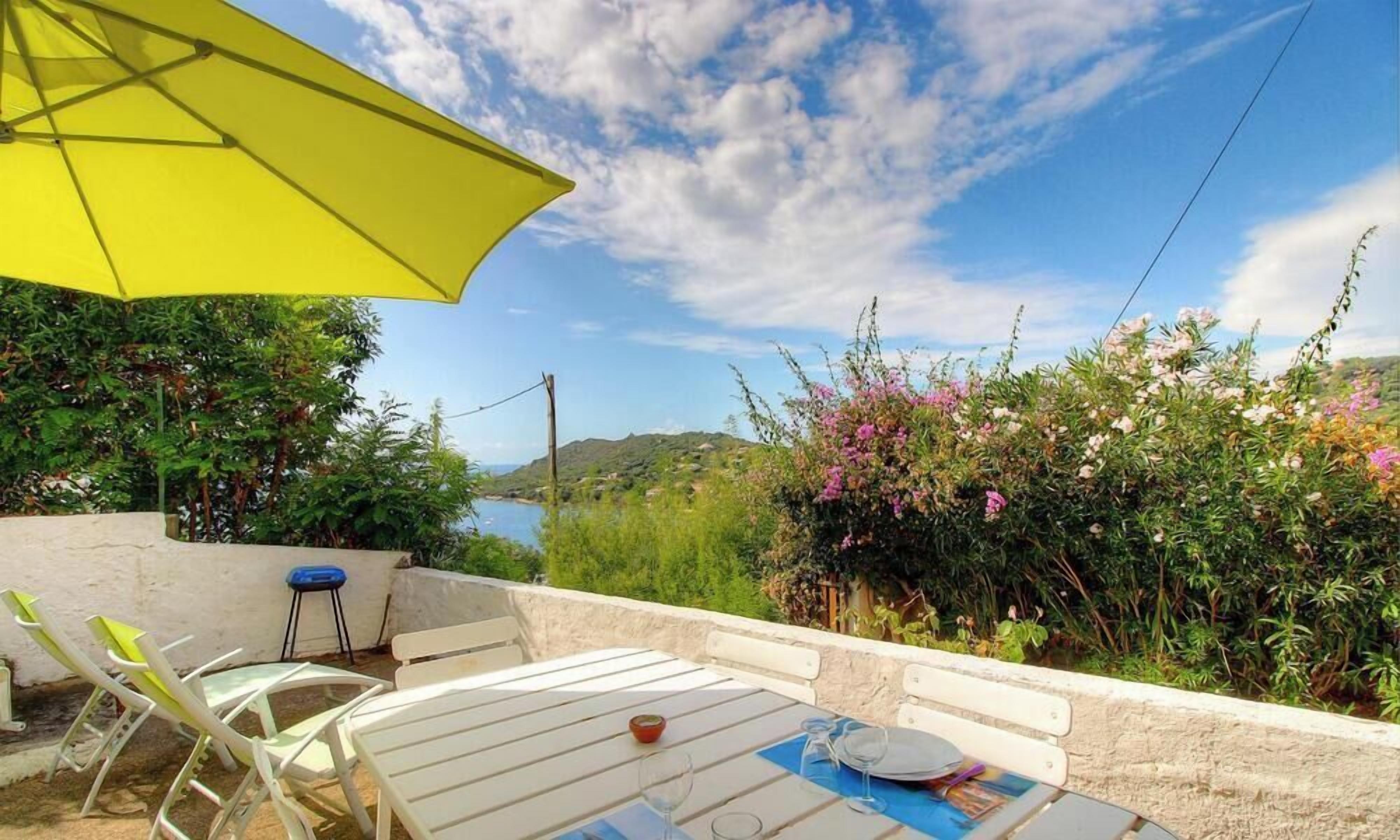 An outdoor patio with a table, chairs, and a yellow umbrella.