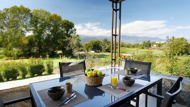 Uma área de refeições ao ar livre com uma mesa posta para dois, rodeada por cadeiras, com vista para uma paisagem exuberante e montanhas ao longe.