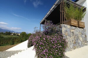 Un bâtiment moderne avec une façade en pierre, une terrasse en bois et un jardin agrémenté de fleurs violettes.