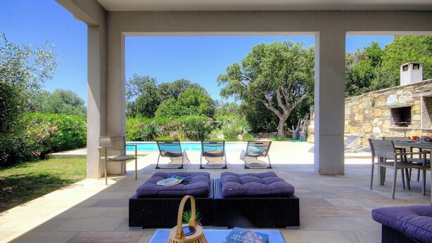 Un espacio exterior techado con sillones, una mesa y un muro de piedra con chimenea.