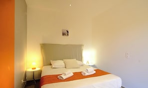 Ein Hotelzimmer mit einem Bett, zwei Nachttischlampen, einer Wandklimaanlage und einem kleinen Tisch mit einer Lampe.