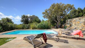 Piscina con sillas de descanso y una pared de piedra.