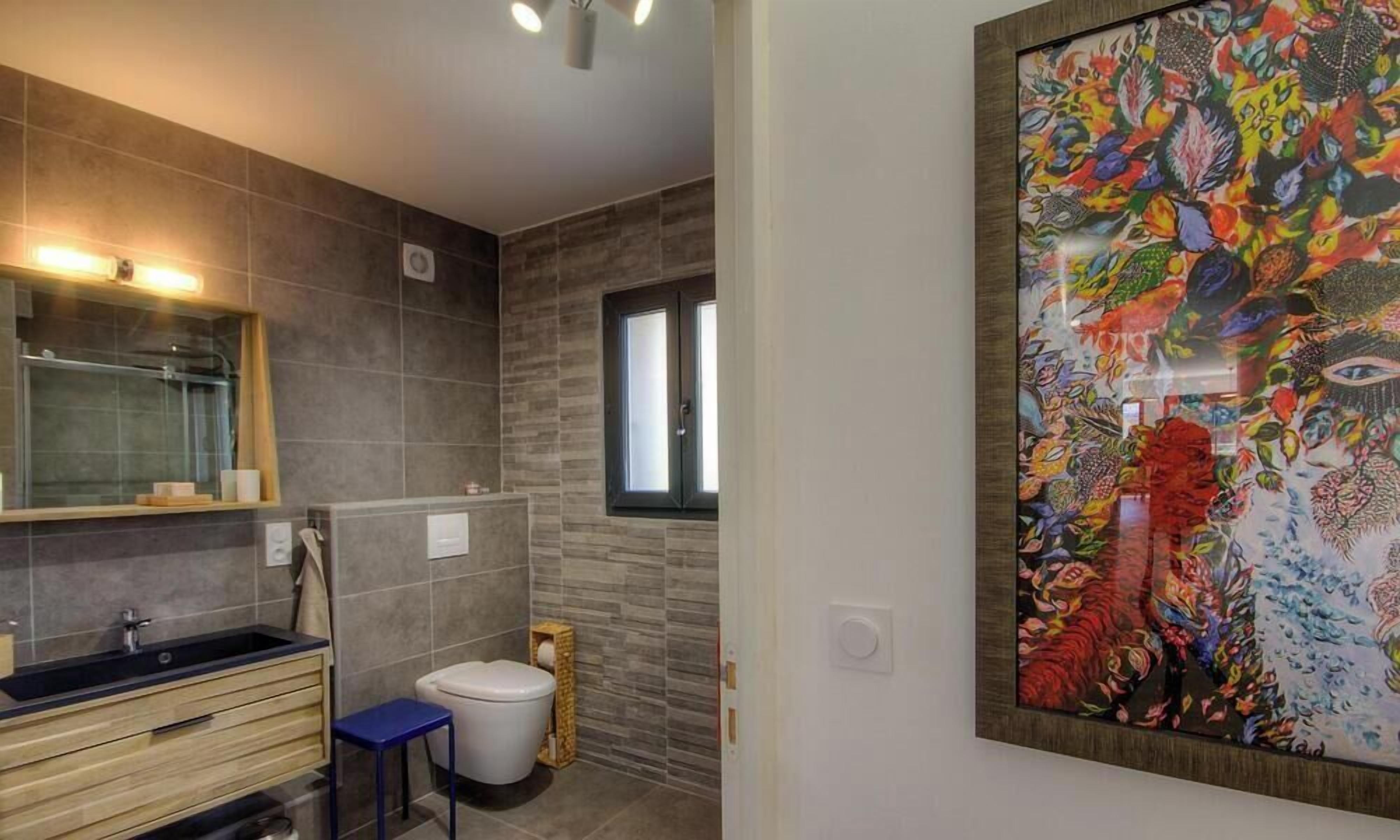 Un bany amb un lavabo modern, vàter i una obra d'art gran emmarcada a la paret.