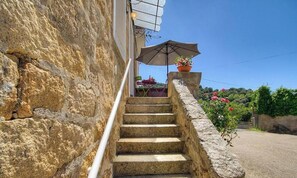 Eine Steintreppe führt zu einer Terrasse mit Tisch und Stühlen, einem Blumentopf und einem wolkenlosen, blauen Himmel.