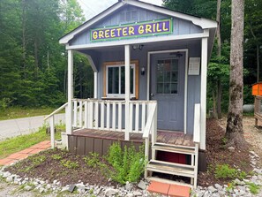 A small, single-story building with a porch, labeled 'GREETER GRILL,' surrounded by trees and a gravel path. - Glamping Yurt at Greeter Falls Campground (Altamont)