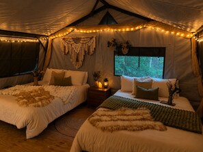A tented accommodation with two beds, string lights, macrame wall decor, and a window with a view of greenery. - Glamping Yurt at Greeter Falls Campground (Altamont)
