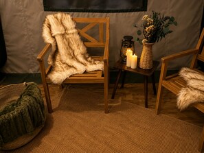 A cozy interior with a fur-covered chair, a small table with candles and a lantern, and a woven basket. - Glamping Yurt at Greeter Falls Campground (Altamont)