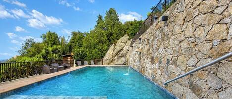 Una piscina con pared de piedra y baranda de metal.