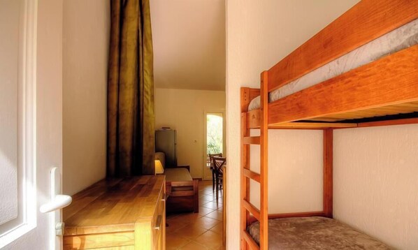 Een kamer met een stapelbed, een houten bureau, een stoel en een raam met gordijnen.