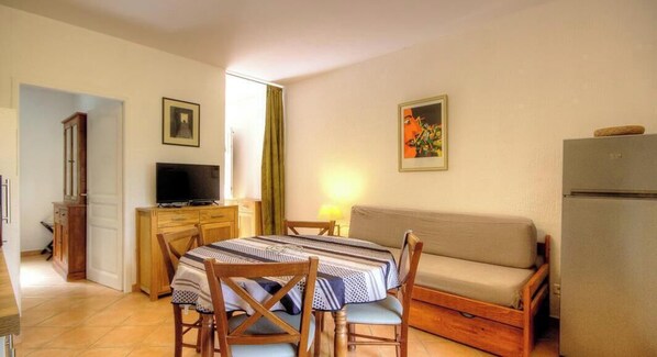 Un espacio habitable pequeño con mesa de comedor, sofá, televisor y refrigerador.