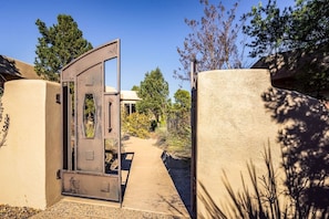 A gated entrance with a metal door, a pathway leading to a building, and surrounding vegetation. - Rolling Sedona Paradise 4 Bdrm, 4.5 BA, Pool (Sedona)