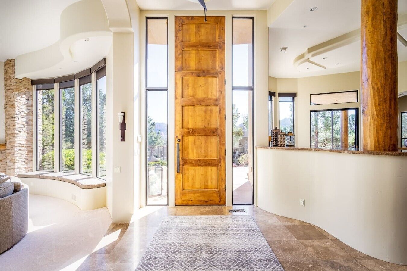 A modern interior with a large wooden door, stone wall, and large windows offering a view of the outdoors.