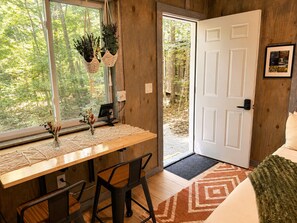 A room with a wooden desk, two chairs, a computer, a door, and a window with plants.