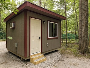 A small, single-story cabin with a door, a window, and a step leading to the entrance.
