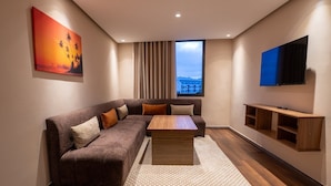 A modern living room with a sectional sofa, a coffee table, a TV, and a window with a view. - OCEAN ROOFTOP HOTEL (El Mansouria)