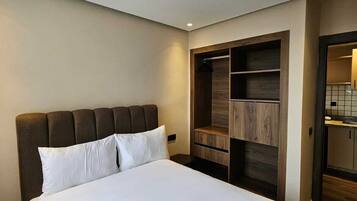 A hotel room with a large bed, a wooden wardrobe, and a small kitchenette.