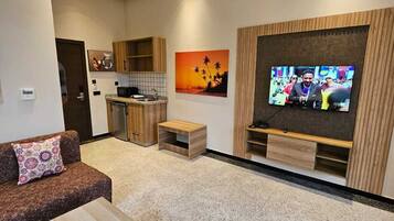 Una sala de estar moderna con sofá, mesa de centro, televisor y zona de cocina.
