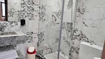 Un baño con ducha de vidrio, paredes de mármol, inodoro blanco y lavamanos con encimera de mármol.