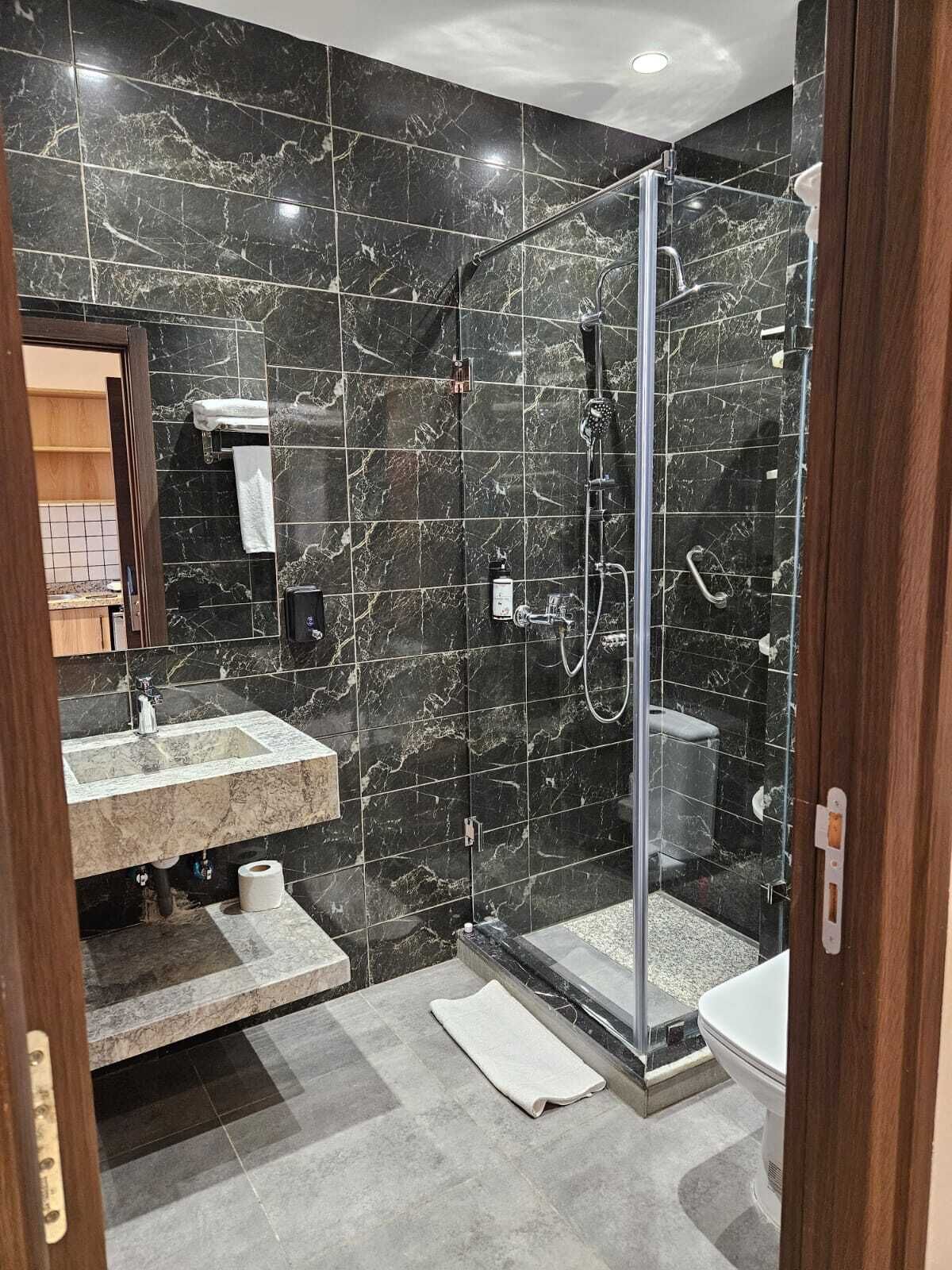 A modern bathroom with a glass-enclosed shower, a marble-tiled wall, a sink, and a toilet.
