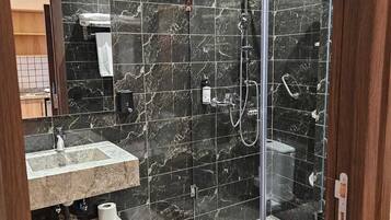 A modern bathroom with a glass-enclosed shower, a marble-tiled wall, a sink, and a toilet.