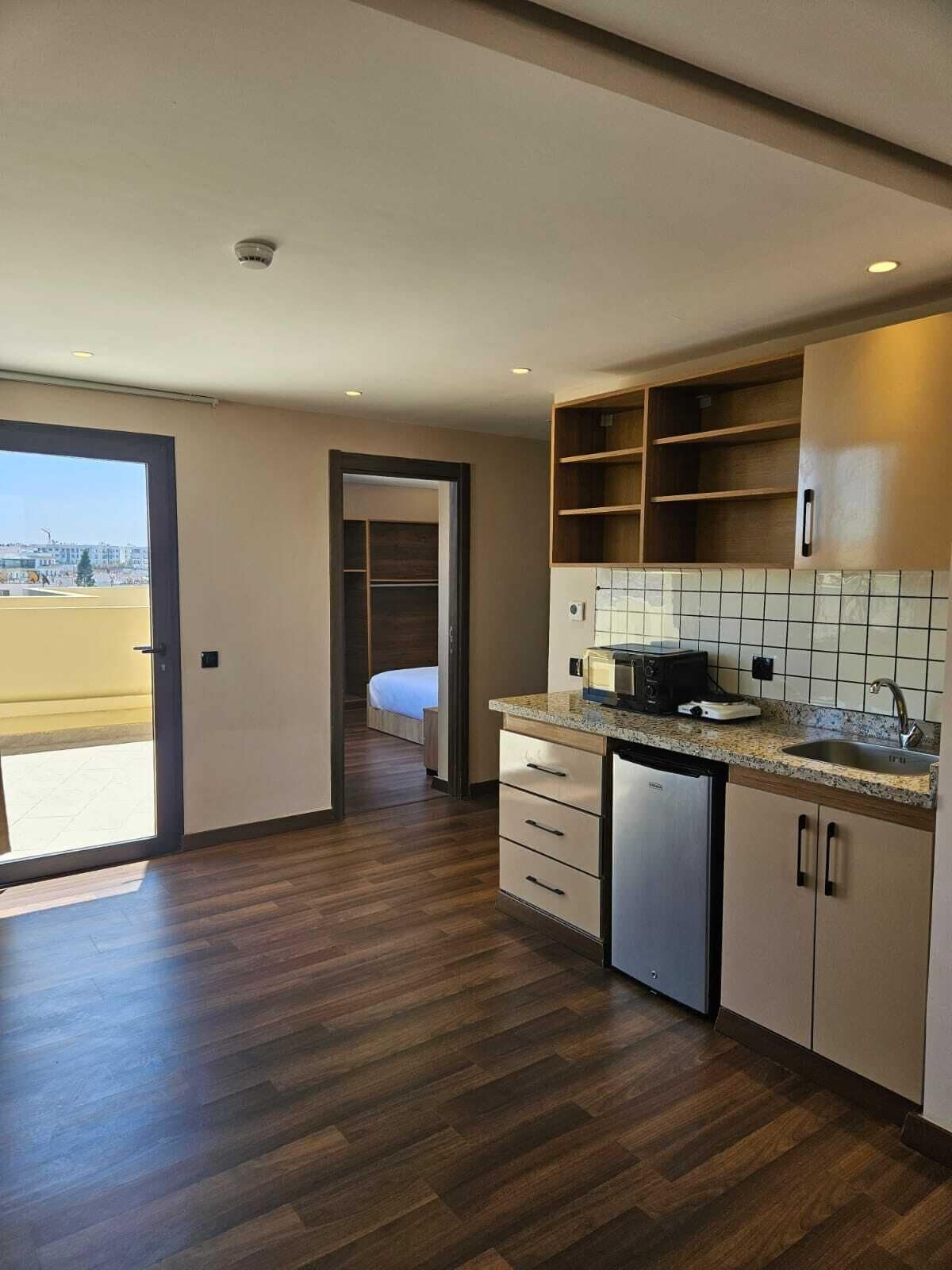 Eine moderne Küche mit Holzschränken, einem eingebauten Geschirrspüler und Blick durch eine offene Tür auf einen Balkon.
