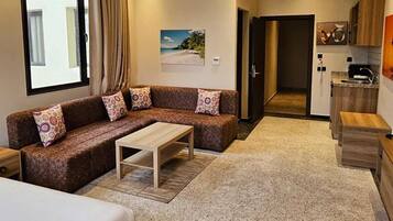 A modern hotel room with a sofa, a small table, a bed, a kitchenette, and a view of the outdoors.