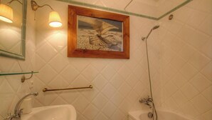 A bathroom with a sink, mirror, shower, and a framed picture on the wall.