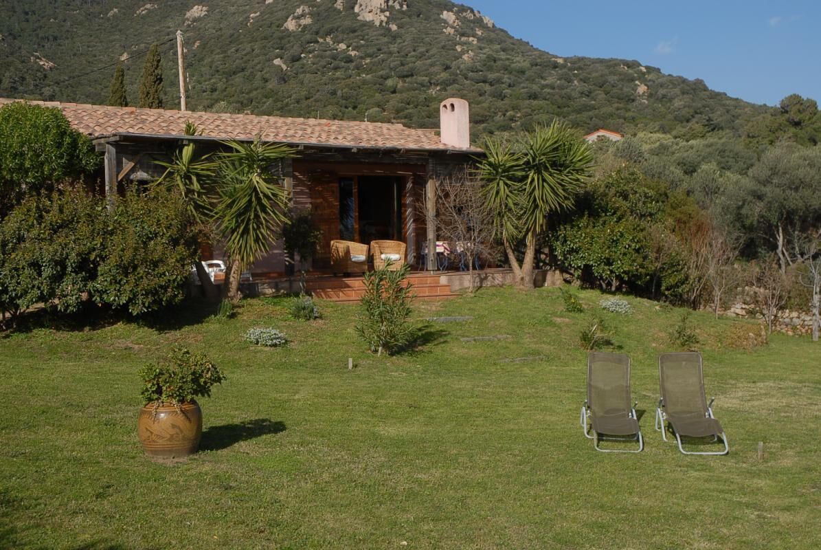 A rustic house with a tiled roof, a porch with chairs, and a lawn with two lounge chairs.