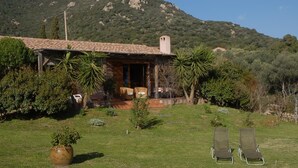 A rustic house with a tiled roof, a porch with chairs, and a lawn with two lounge chairs.