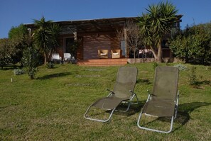 Ein Haus mit einer Veranda, zwei Liegestühlen und einem Garten mit verschiedenen Pflanzen.