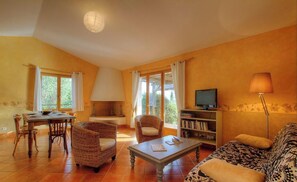Ein Wohnzimmer mit Esstisch, Korbstühlen, einer Couch, einem Fernseher und einem Bücherregal.