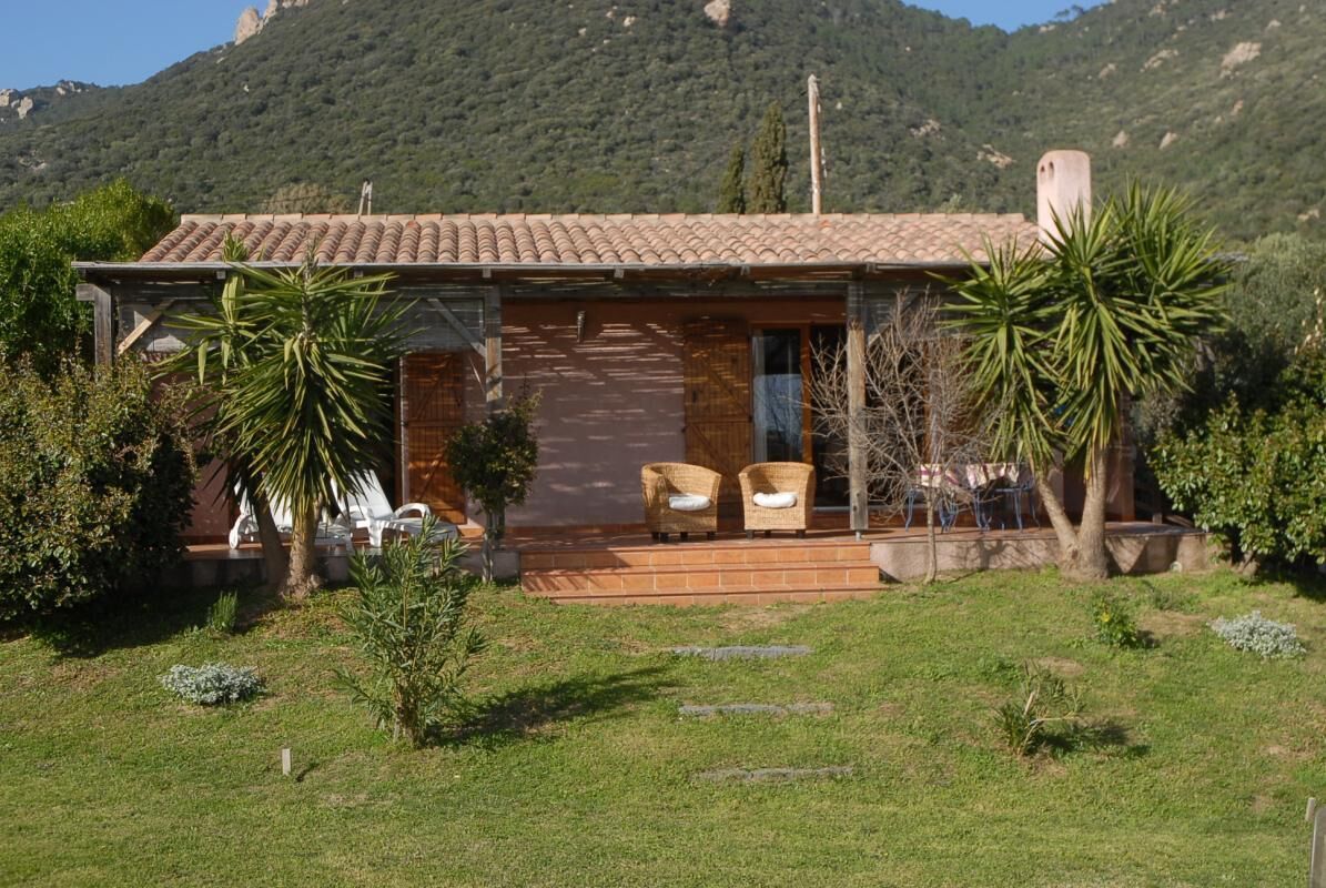 A house with a tiled roof, a porch with wicker chairs, and a mountain backdrop.