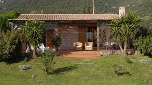 A house with a tiled roof, a porch with wicker chairs, and a mountain backdrop.