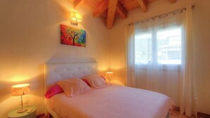 A bedroom with a bed, two bedside lamps, a painting on the wall, and a window with curtains. - Villa Marie - FIGARI (FIGARI)
