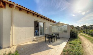 Eine Terrasse mit Tisch und Stühlen, eine Glastür zum Verschieben und ein überdachter Bereich mit einem Fenster.