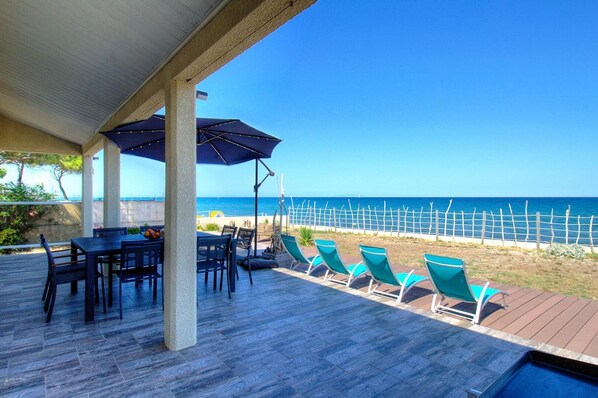 Une terrasse couverte avec une table et des chaises, une piscine et une vue sur la mer.