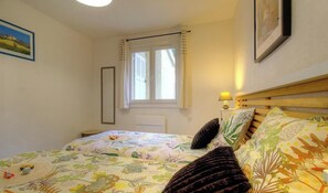 Une chambre à coucher avec un lit, une fenêtre avec des rideaux, une lampe de chevet et un tableau encadré au mur.