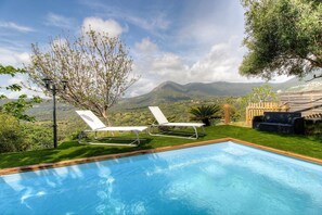 Ein Pool mit zwei Liegestühlen, einer Holzterrasse und Blick auf Berge.